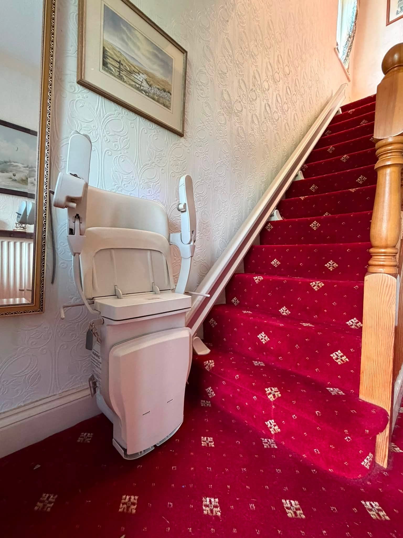 A cream stairlift fitted to a red-carpeted staircase in a home